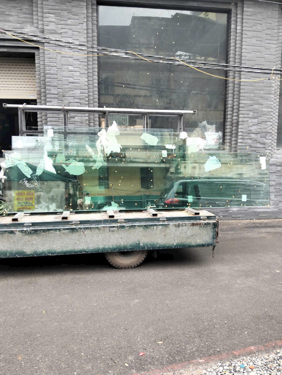 Các tấm kính lớn được vận chuyển trên xe tải trước một tòa nhà mặt tiền ốp đá xám